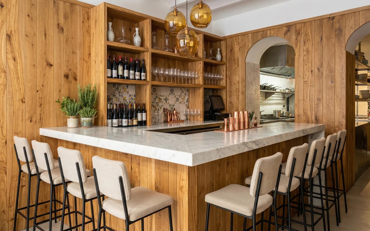 Barra de mármol con taburetes y estantería de madera de olivo